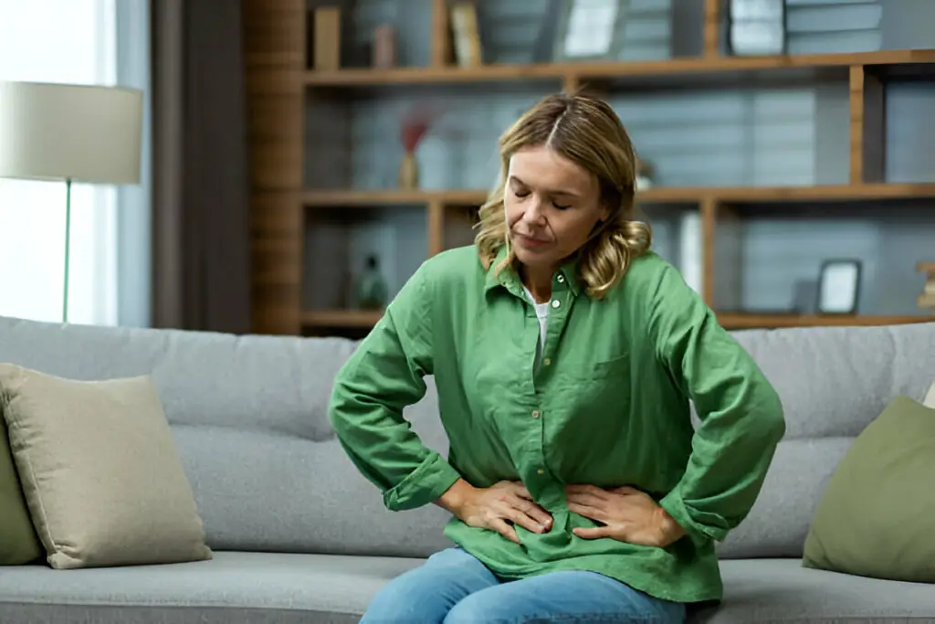Woman holding her bloated stomach indoors, showing signs of gut discomfort related to the gut hormone connection.